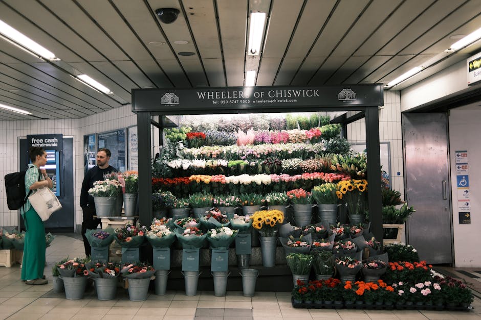 A floral display at Wheeler of Chiswick inside a subway or underground station, showcasing a variety of fresh flowers arranged in bouquets and buckets. The arrangement includes colorful blooms such as